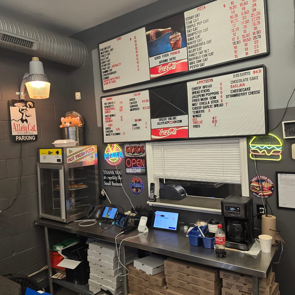 A small, busy restaurant kitchen with menus, a pizza oven, and order tablets on a counter.