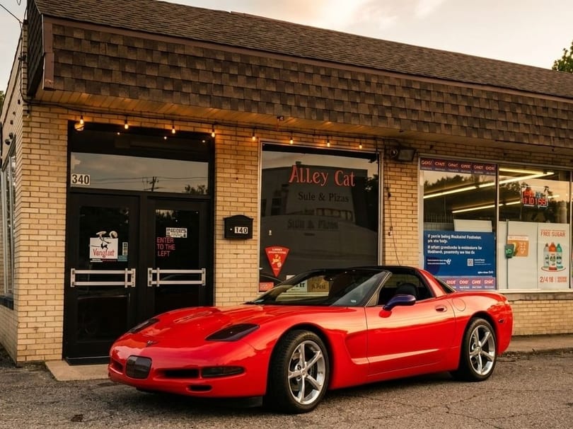A red sports car parked in front of Alley Cat restaurant, a brick building with large windows.