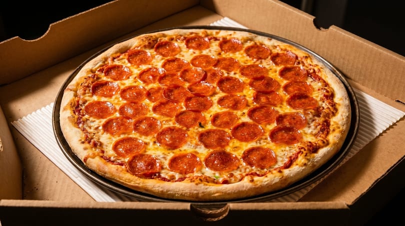 A large, hot pepperoni pizza in a cardboard delivery box, ready to be served.