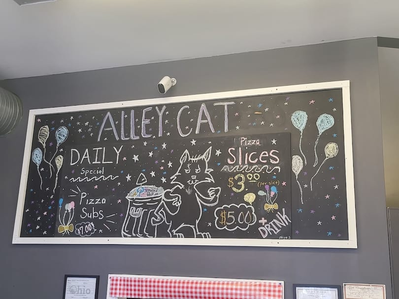 Chalkboard menu for Alley Cat restaurant, featuring pizza slices, subs, and a drink special.